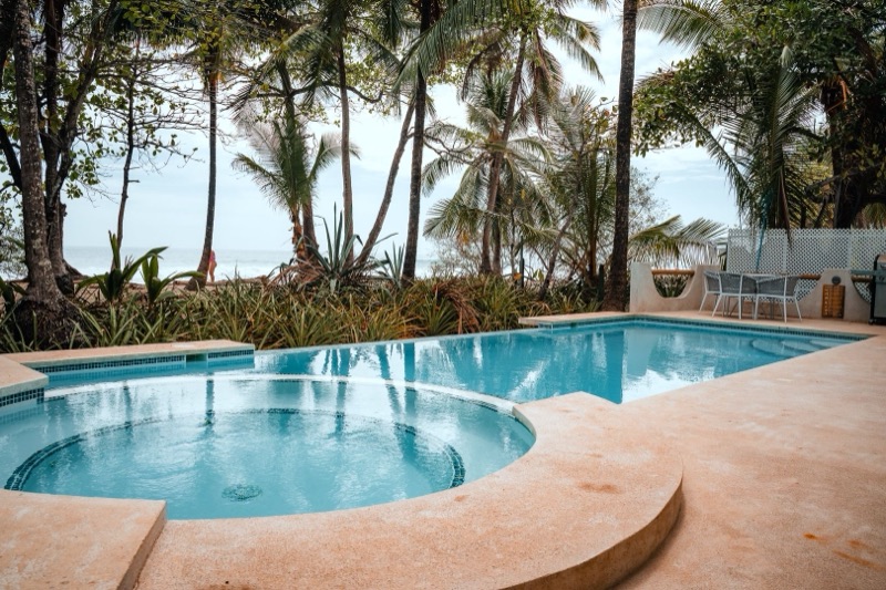 Pool and hot tub with palm trees and the beach behind at Hotel Tropico Latino